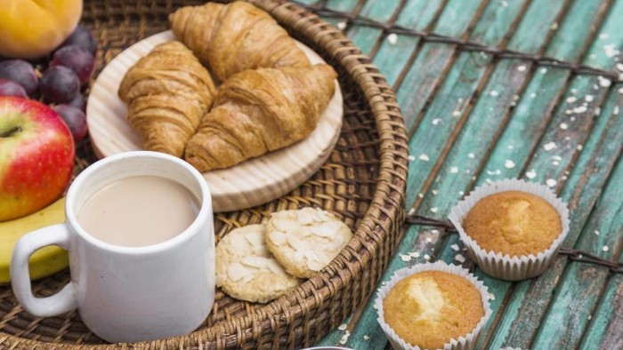 Frische Gebäckstücke, Obst, Muffins und Haferbrei in einem rustikalen Outdoor-Frühstücksaufbau auf einem Holztisch.