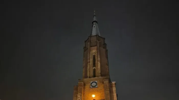 Ein beleuchteter Kirchturm bei Nacht mit Uhr und Weihnachtslichtern