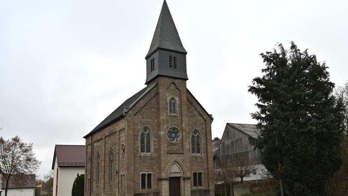 Idyllische Steinkirche mit steilem Turm und Bogenfenstern in einem ruhigen Dorf.