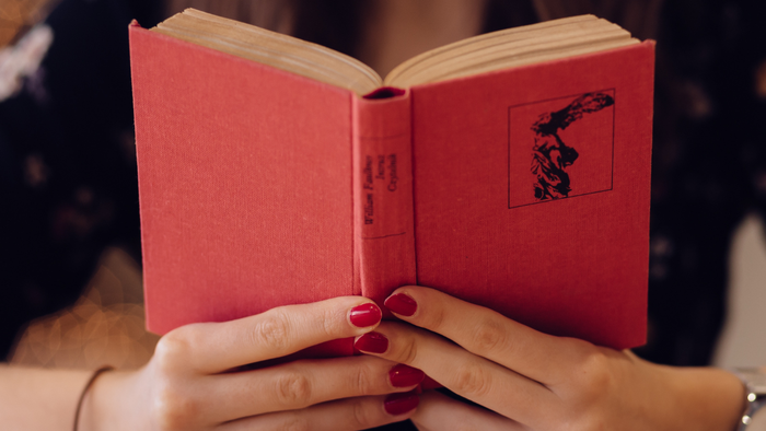 Eine Person hält ein aufgeschlagenes rotes Buch mit schwarzem Cover und liest es.