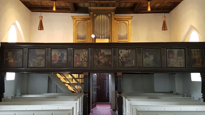 Historisches Kircheninneres mit hölzernen Kirchenbänken, Buntglasfenstern und einer prunkvollen Orgel.