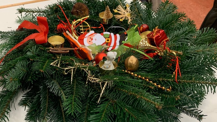 Aufwendig verzierter Weihnachtskranz mit festlichen Schmuckstücken, Weihnachtsmann und roten Schleifen auf grüner Tannengrundlage.
