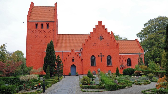 Historisk rødstenskirke med et højt tårn og en velholdt havegang.