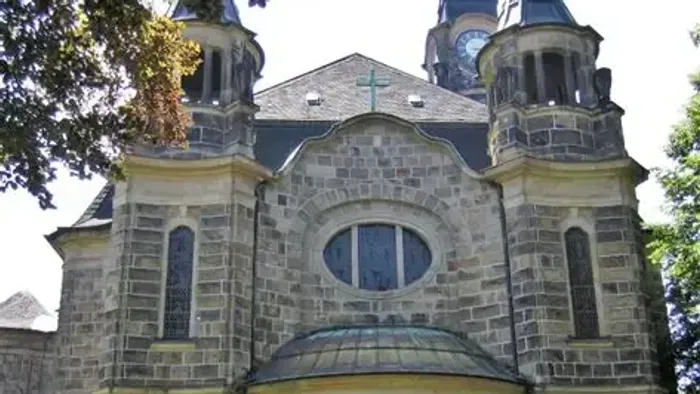 Historische Steinkirche mit Zwillingstürmen, bogenförmigem Eingang und einem runden Buntglasfenster über der Tür.