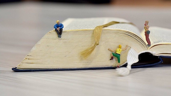 Kleine Figuren posieren verspielt auf einem offenen Buch wie ein improvisiertes Boot auf einem Tisch.