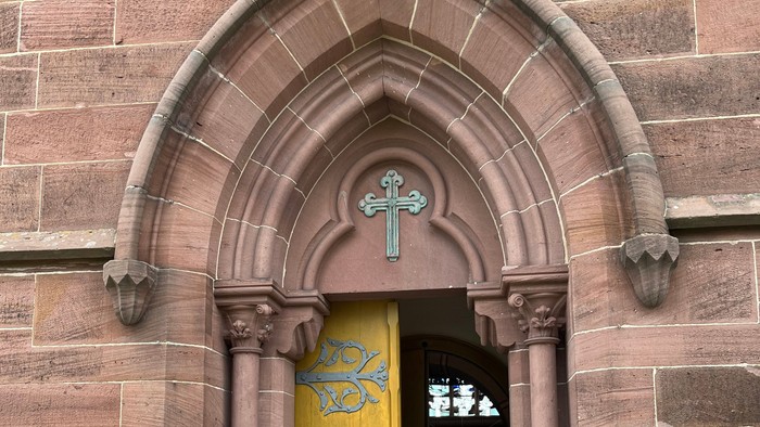 Kircheneingang mit bogigem Türbogen und gelber Tür.
