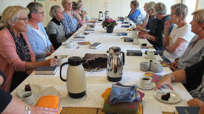 En gruppe kvinder sidder ved et langt bord med kaffe og papirer.