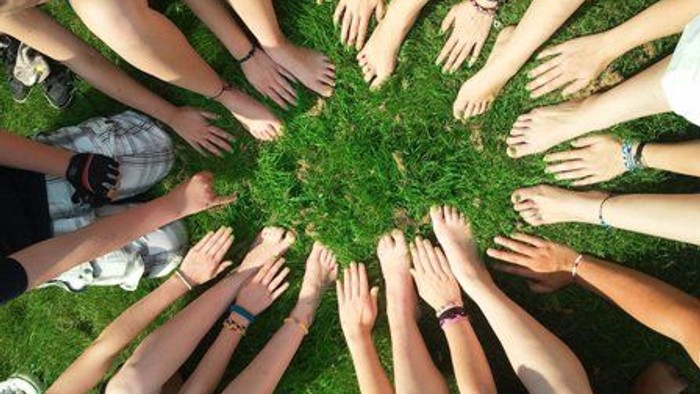 Eine Gruppe von Händen und Füßen von Menschen, die im Kreis um ein Stück Gras angeordnet sind.
