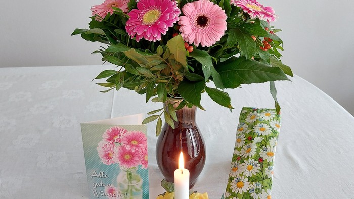 Ein Blumenstrauß in einer Vase auf einem Tisch mit einer Kerze und einer Karte