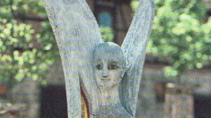 Eine hölzerne Statue eines Engels namens Michael steht friedlich in einem Garten im Freien.