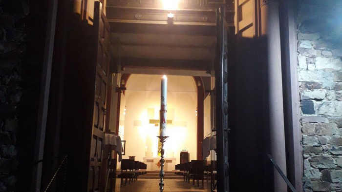 Eine Osterkerze vor einem Kirchportal, mit Blick in eine beleuchtete Kirche