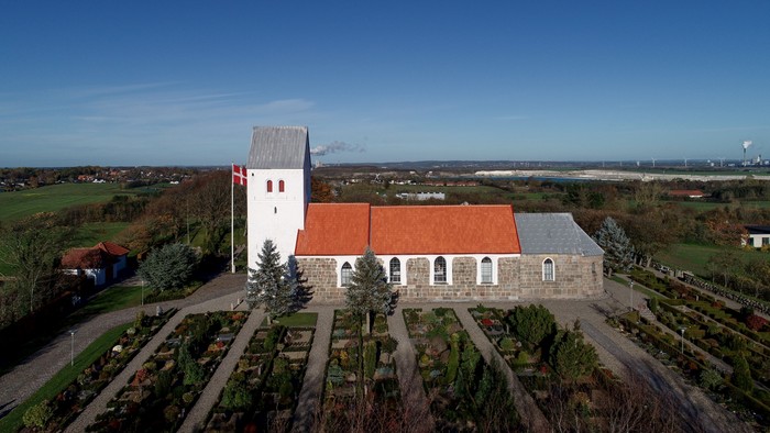 En lille kirke med rosengård og udsigt over landskabet
