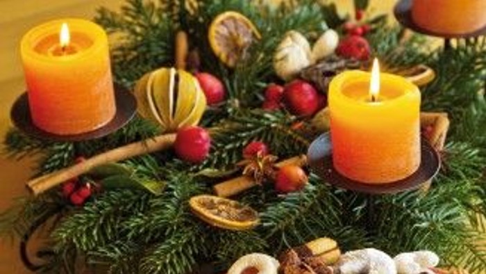 Ein festlicher Tischschmuck mit Kerzen, Tannenzweigen, Orangen und Plätzchen.