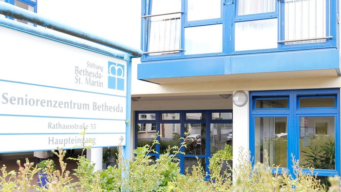Blauer gerahmter Eingang des Seniorenzentrums mit dem Schild „Seniorenzentrum Bethesda St. Martin“ und üppigem Grün im Vordergrund.