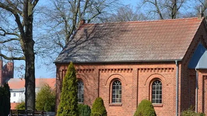 Backsteinkirche mit rotem Dach, umgeben von Grabsteinen und Bäumen.