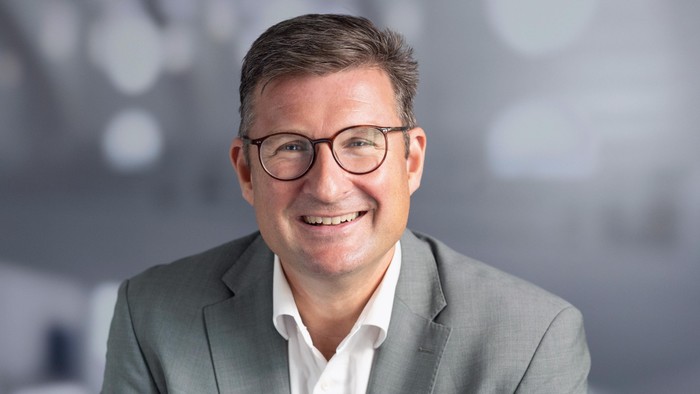 Professioneller Mann mit Brille in einem hellgrünen Sakko, der in die Kamera lächelt.