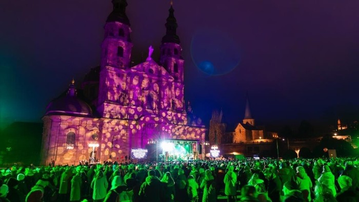 Eine große Menschenmenge versammelte sich nachts vor einem beleuchteten historischen Gebäude.