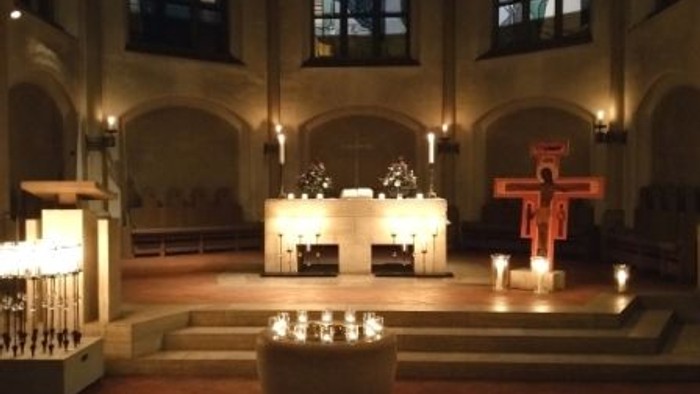Elegante Kircheninnenausstattung mit kerzenbeleuchtetem Altar, Buntglasfenstern und einem markanten Kruzifix.