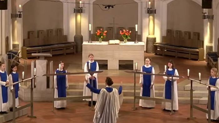 Ein Chor tritt während eines Gottesdienstes in einer Kirche auf und steht um einen zentralen Altar mit Kerzen herum.