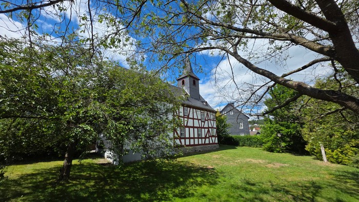 Fachwerkkirche im Hintergrund. Bäume im Vordergrund. Grüne Wiese 
