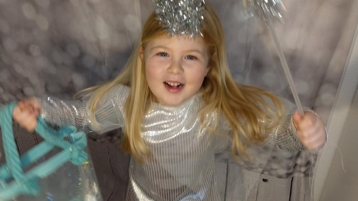 Ein kleines Mädchen in silbernem Kleid spielt fröhlich mit einem blauen Gegenstand.