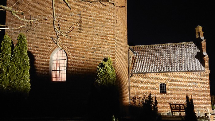 En mørk nattehavende kirke med klokketårn og en blå klokke.