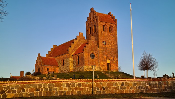 Gamle kirke i rød tegl med tårn og mur.