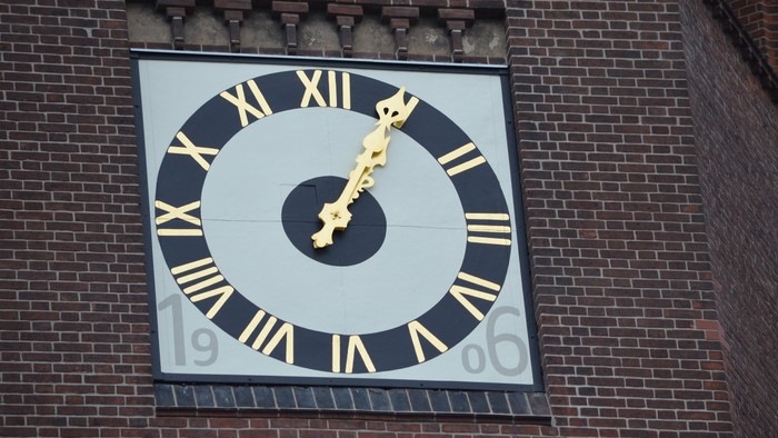 Großer Uhrturm mit goldenen Zeigern und römischen Ziffern an Backsteinmauer