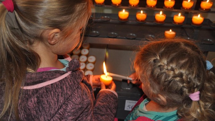 Zwei Mädchen zünden Kerzen in einer Kirche an.