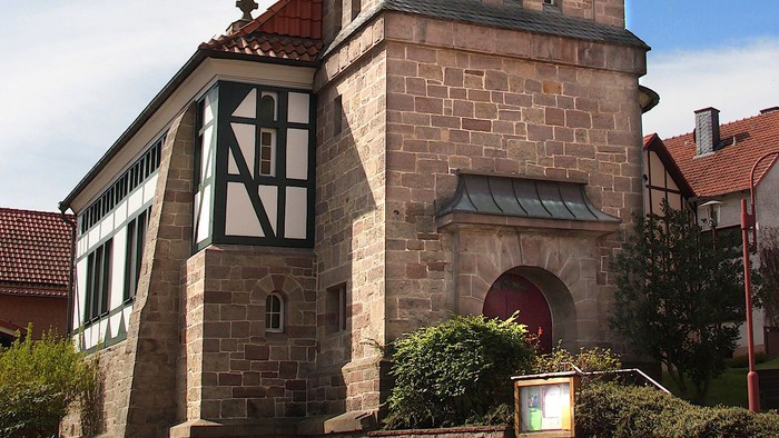 Außenansicht der evangelischen Kirche in Arenborn. Natursteinturm mit schieferverkleideter, geschwungener Haube.