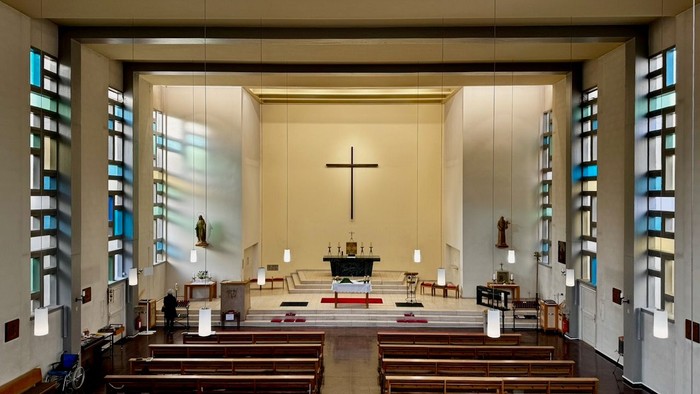 Moderne Kircheninnenausstattung mit hölzernen Kirchenbänken, Kreuz und bunten Glasfenstern.