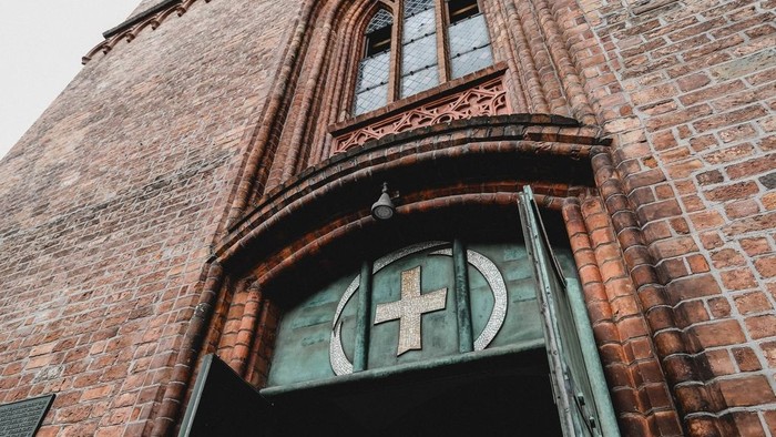 Das Bild zeigt den Eingang einer Kirche mit einem Kreuz über der Tür.