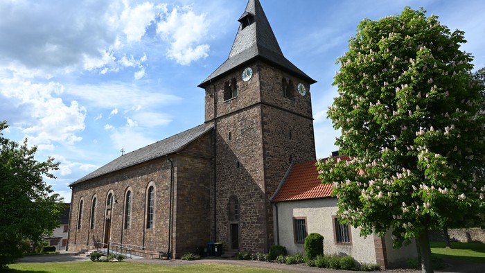 Idyllische Steinkirche mit Uhrturm, umgeben von einer üppigen, grünen Rasenfläche unter klarem Himmel.
