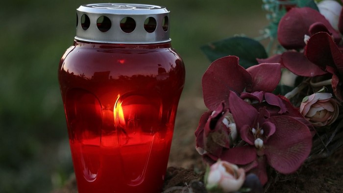 Eine rote Kerze mit Blumen auf einem Grab.