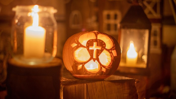 Kerzen in Gläsern und ein geschnitzter Kürbis, erleuchtet, mit Kreuz