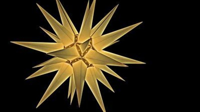 Ein gelber, sternförmiger Weihnachtsstern vor schwarzem Hintergrund.