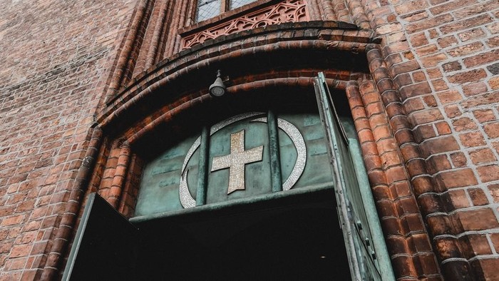 Das Bild zeigt den Eingang einer Kirche mit einem Kreuz über der Tür.