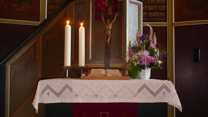 Eleganter Altar mit einem Kruzifix, Kerzen, Blumen und einem kreuzbestickten Tuch.