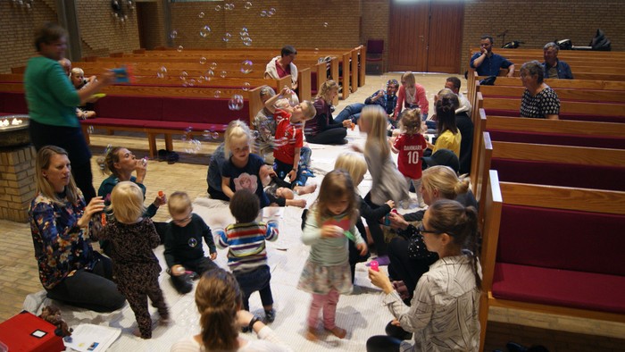 Børn og voksne samles i kirke for aktivitet med boble.