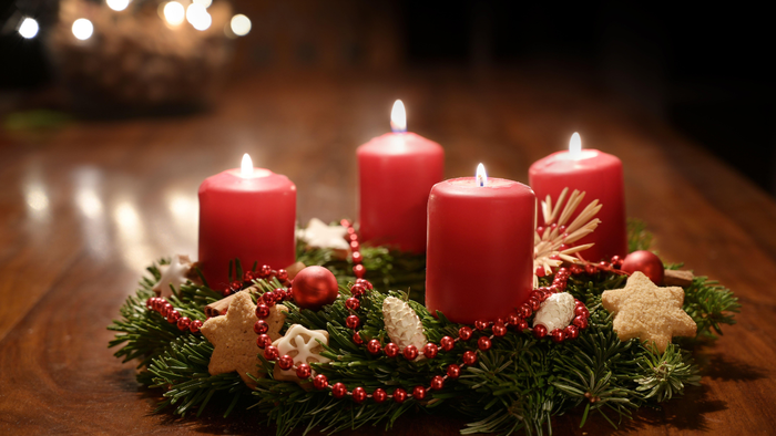 Vier brennende rote Kerzen, umgeben von Weihnachtsdekorationen auf einem Holztisch.