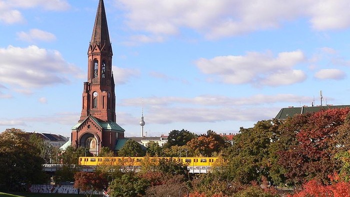 Kirchturm mit spitzem Dach vor Herbstbäumen und blauen Himmel