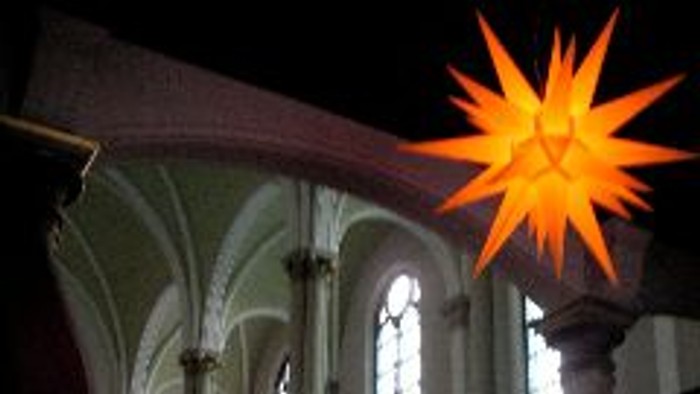 Eine hell erleuchtete Sternendekoration erhellt das schwach beleuchtete, gewölbte Innere einer Kirche oder Kathedrale.