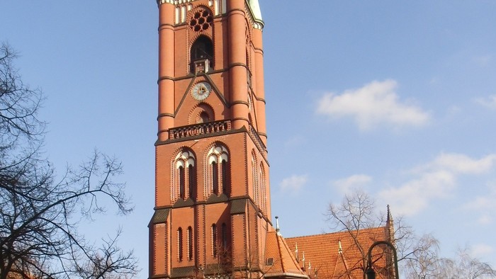 Großer roter Backsteinturm mit spitzem Dach und Uhr.