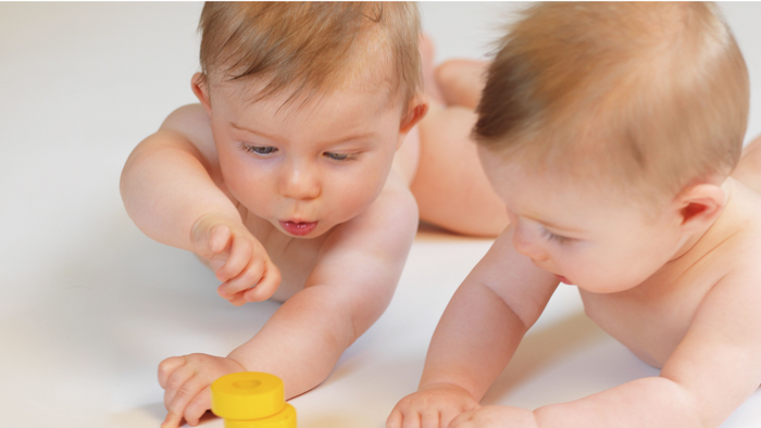 Zwei Babys spielen mit bunten Stapeltürmen auf einer hellen Oberfläche.