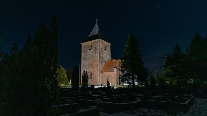 Aftenbillede af Stenderup Kirke. Kirken er oplyst mod den mørkeblå nattehimmel.