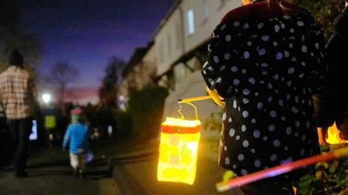 Menschen gehen nachts mit leuchtenden Laternen und glühenden Geräten durch eine schwach beleuchtete Straße.