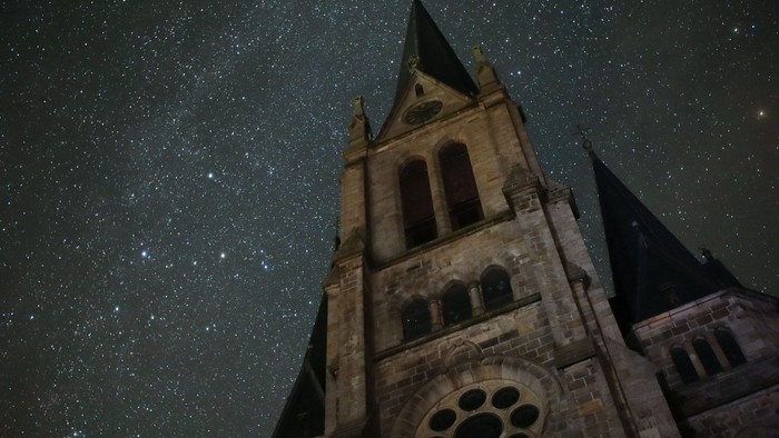 Ein hoher Kirchturm erhebt sich gegen den sternenklaren Nachthimmel.