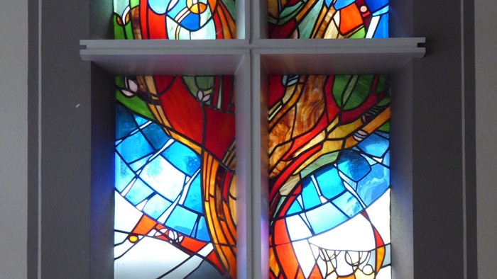 Buntglasfenster mit lebendiger abstrakter religiöser Kunst, das wirbelnde Farben und Figuren darstellt.