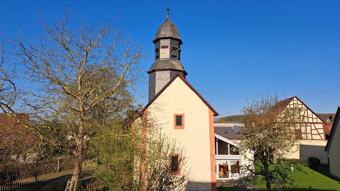 Eine malerische Kirche mit Glockenturm vor einem klaren blauen Himmel und traditionellen Fachwerkhäusern.
