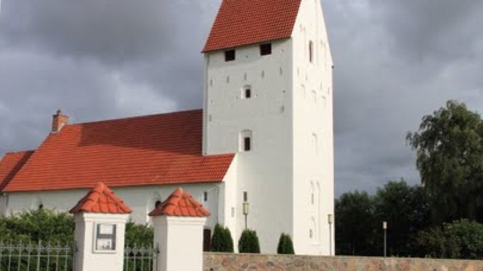 Et hvidt tårn med rødt tag og en indhegnet have.
